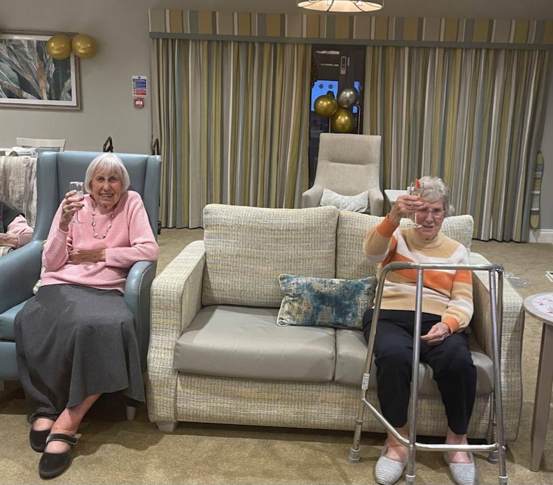 two residents sat down smiling with a glass in their hand