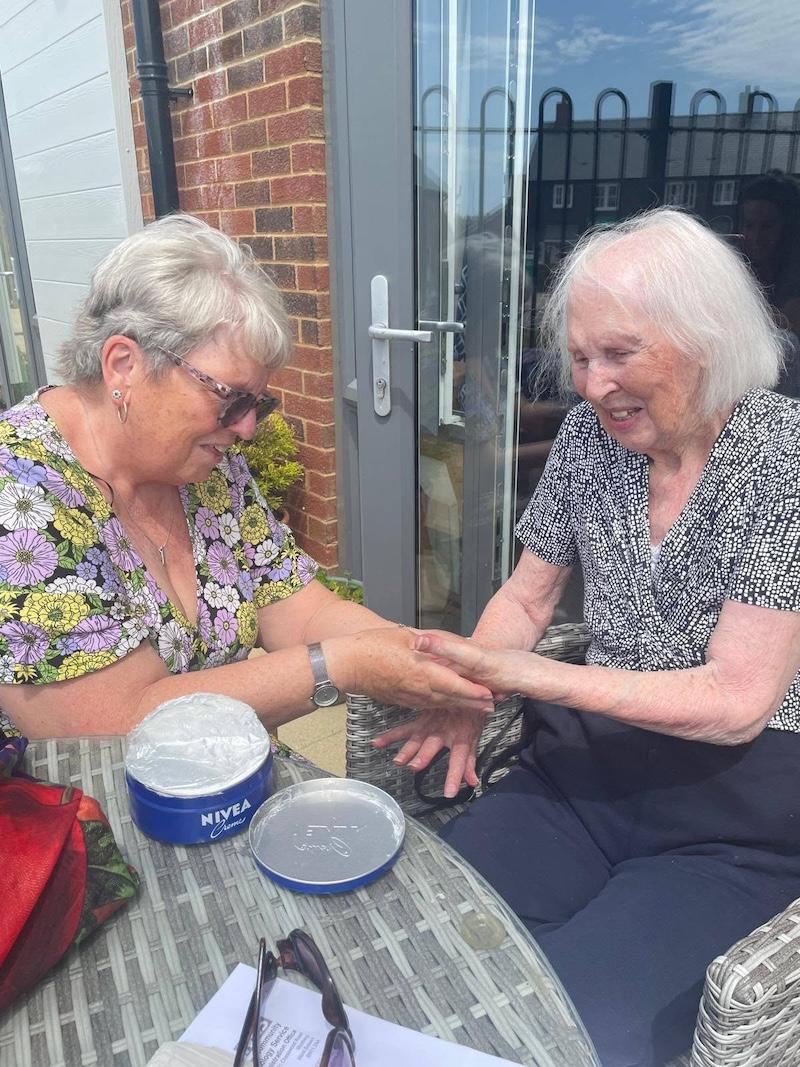 resident sat outside with carer having cream rubbed onto her hands