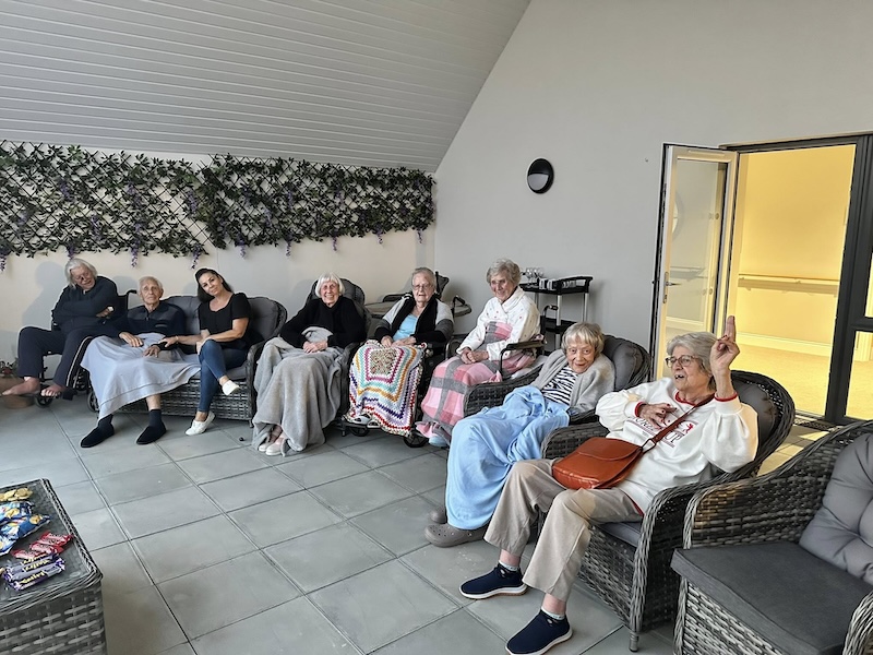 residents sat in chairs on the balcony with blankets on watching a firework display
